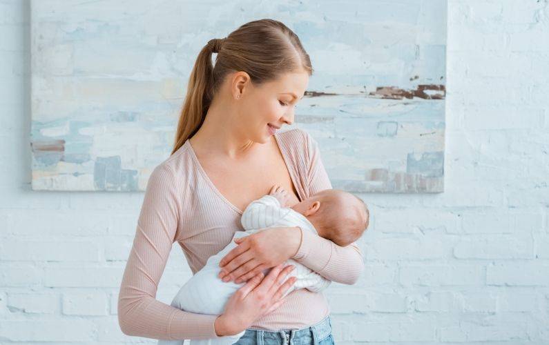 mom smiling while holding breastfeeding her baby