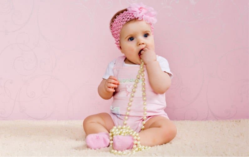 baby girl wearing pink while holding a necklace with a pink background