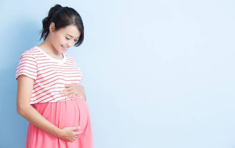 pregnant mom smiling while holding belly with blue background
