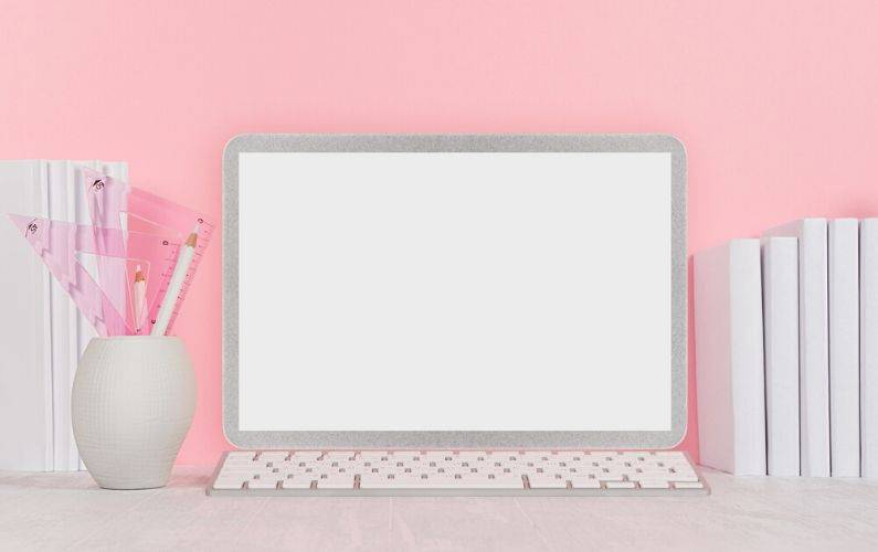 silver computer monitor with keyboard on a desk in front of a pink wall