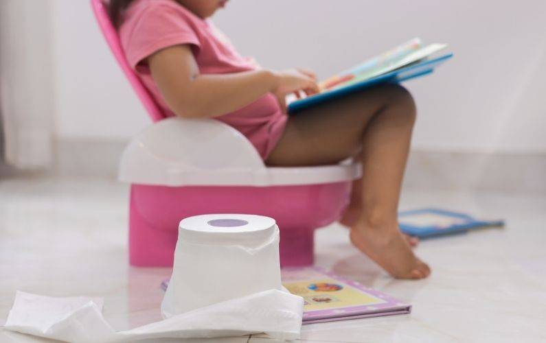 little girl sitting on a pink potty chair with toilet paper