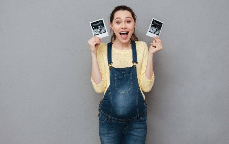 happy pregnant woman holding ultrasound photos