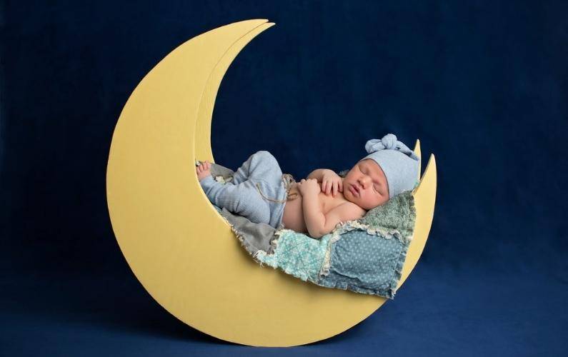 sleeping baby on a crescent moon wearing blue clothes