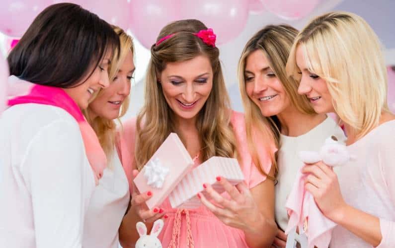 a group of women watching someone open their baby shower prize